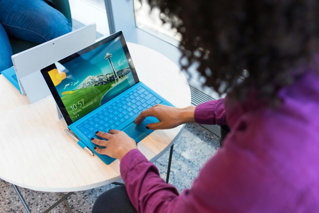 A woman with curly hair works on a laptop indoors with a Seattle skyline on screen.